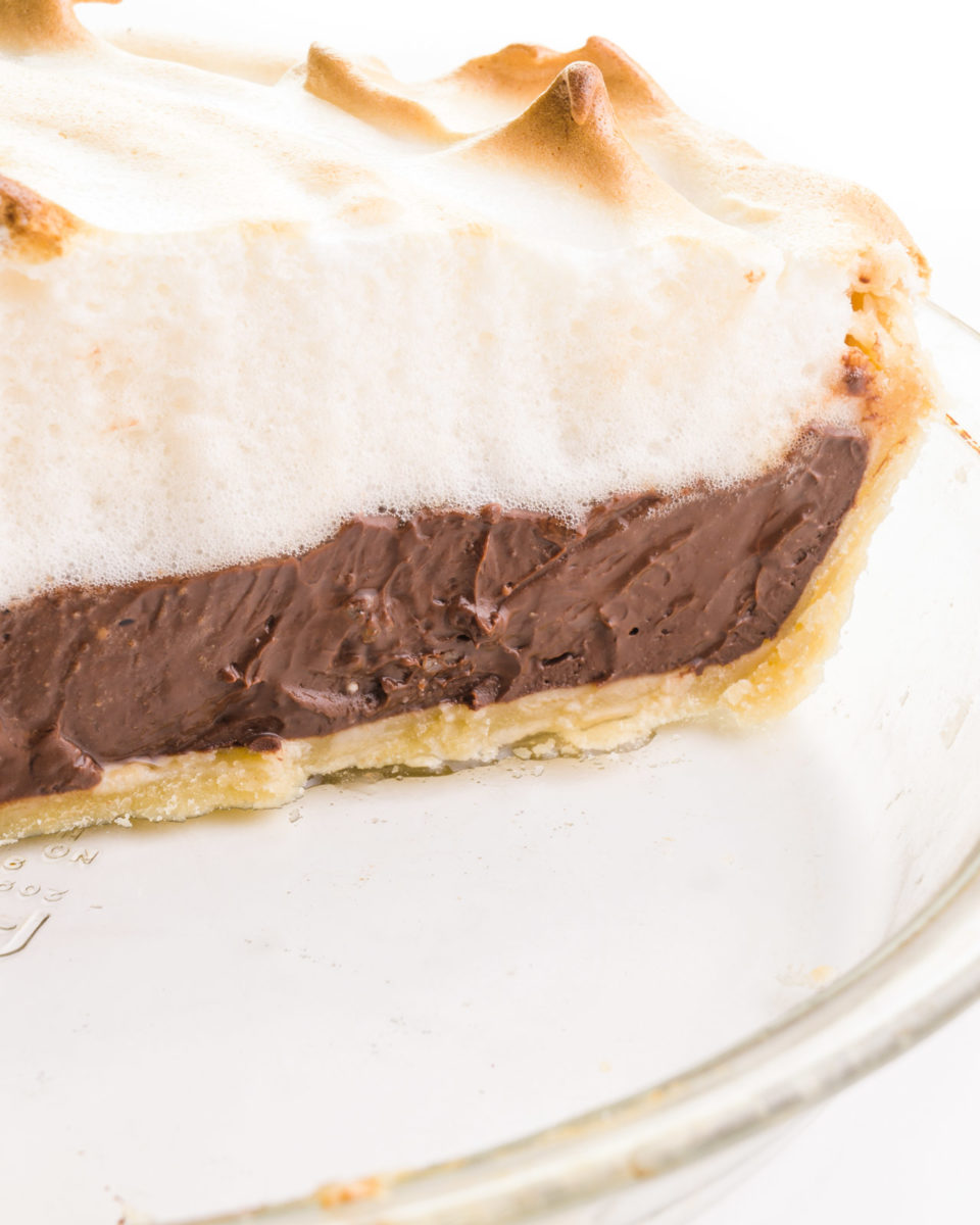 Looking into a pie pan with a vegan chocolate meringue pie, showcasing the crispy crust, creamy chocolate filling, and lots of vegan meringue on top with golden tips.