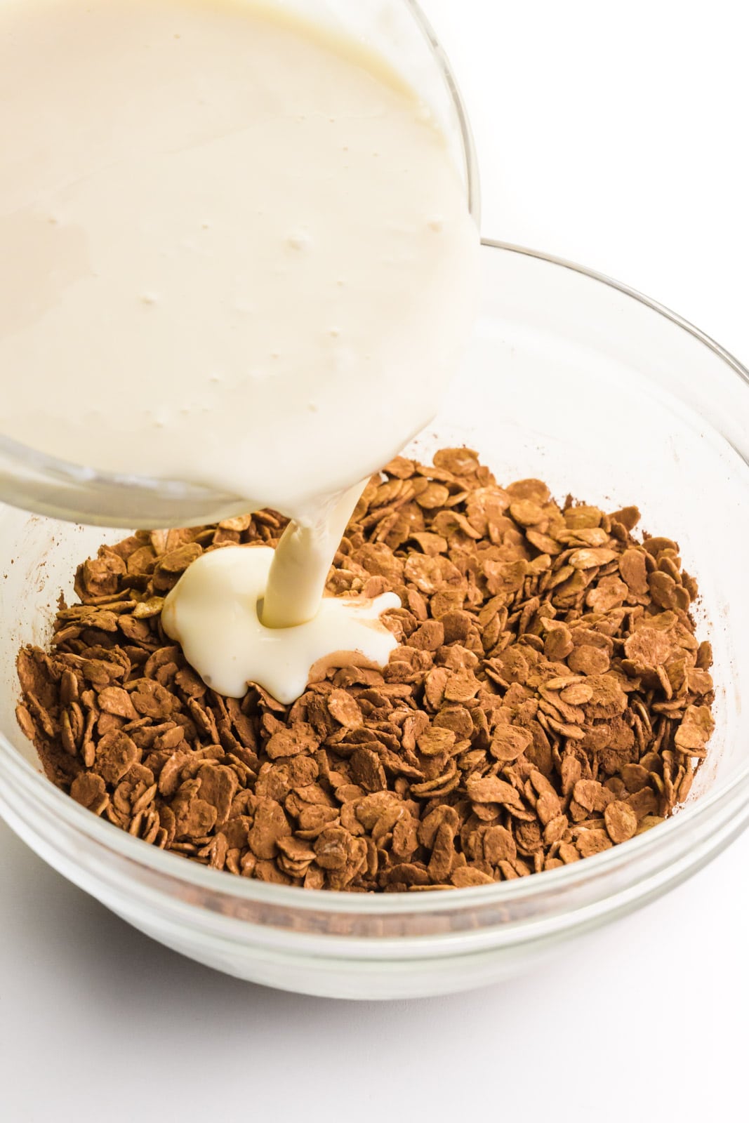 A creamy milk mixture is being poured into a bowl with oats stirred together with cocoa powder.