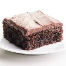 A piece of chocolate zucchini cake sits on a plate. It has frosting on top.