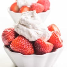 Two bowls of strawberries have coconut milk whipped cream on top. One is sitting in from the other.