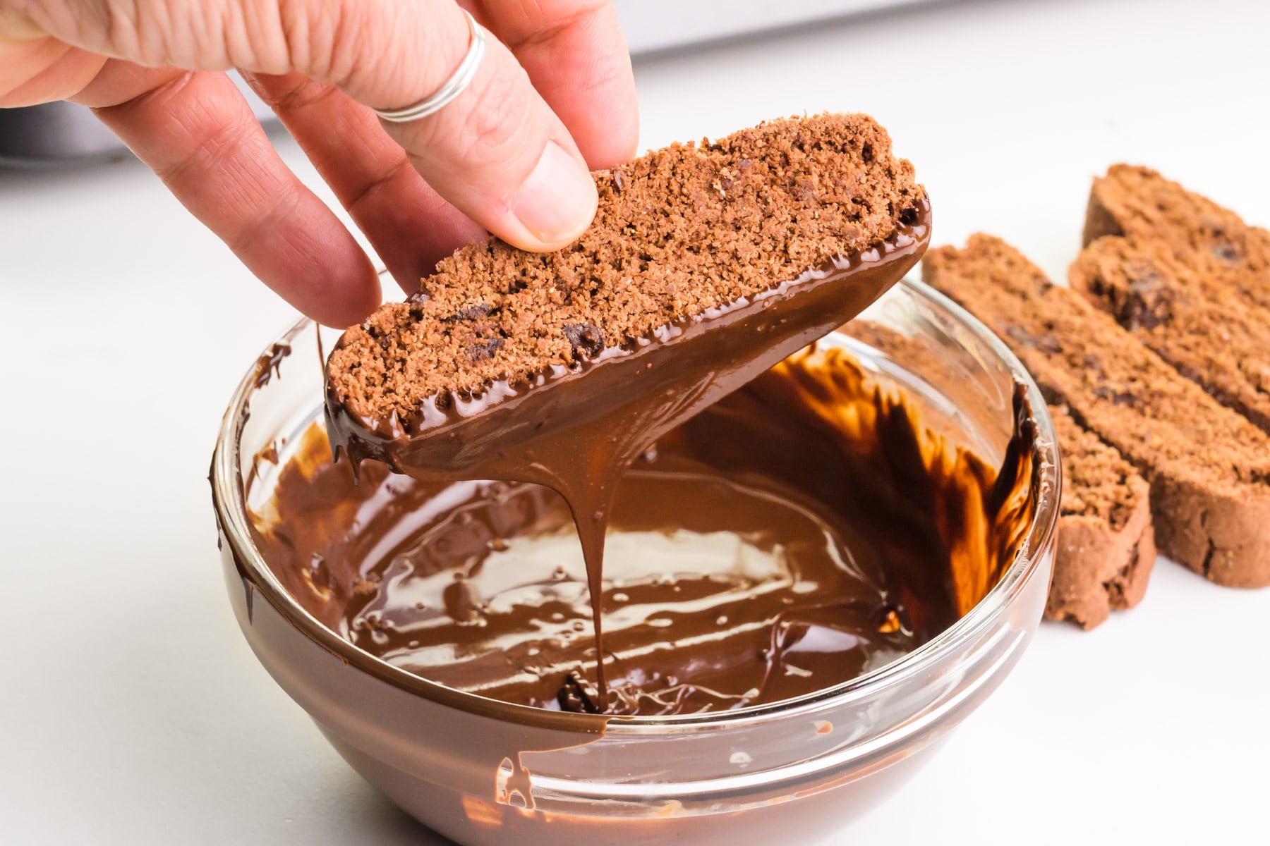 A hand holds a crisp chocolate cookie, dipping it in melted chocolate.
