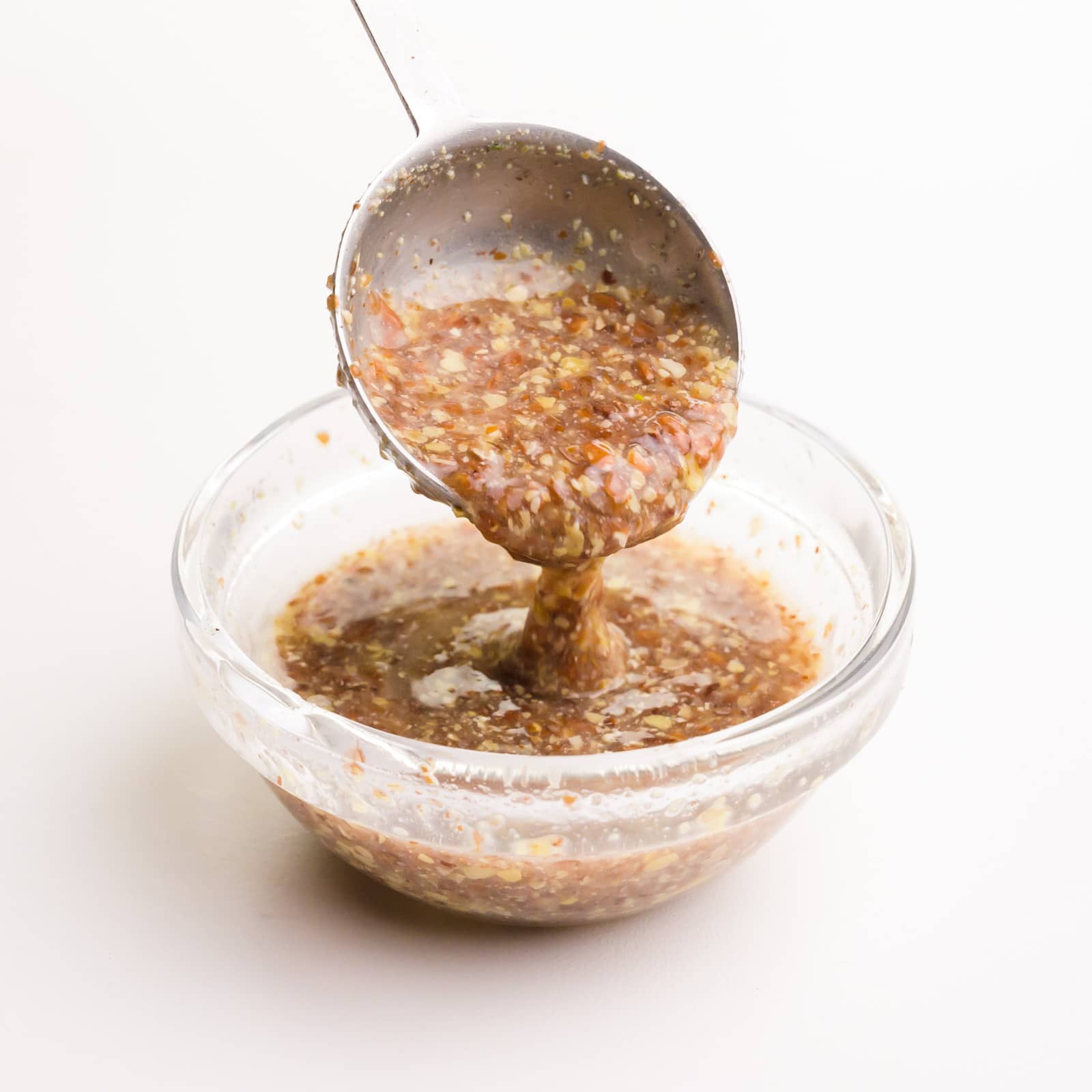 A measuring spoon drizzles a flax egg mixture into a small glass bowl