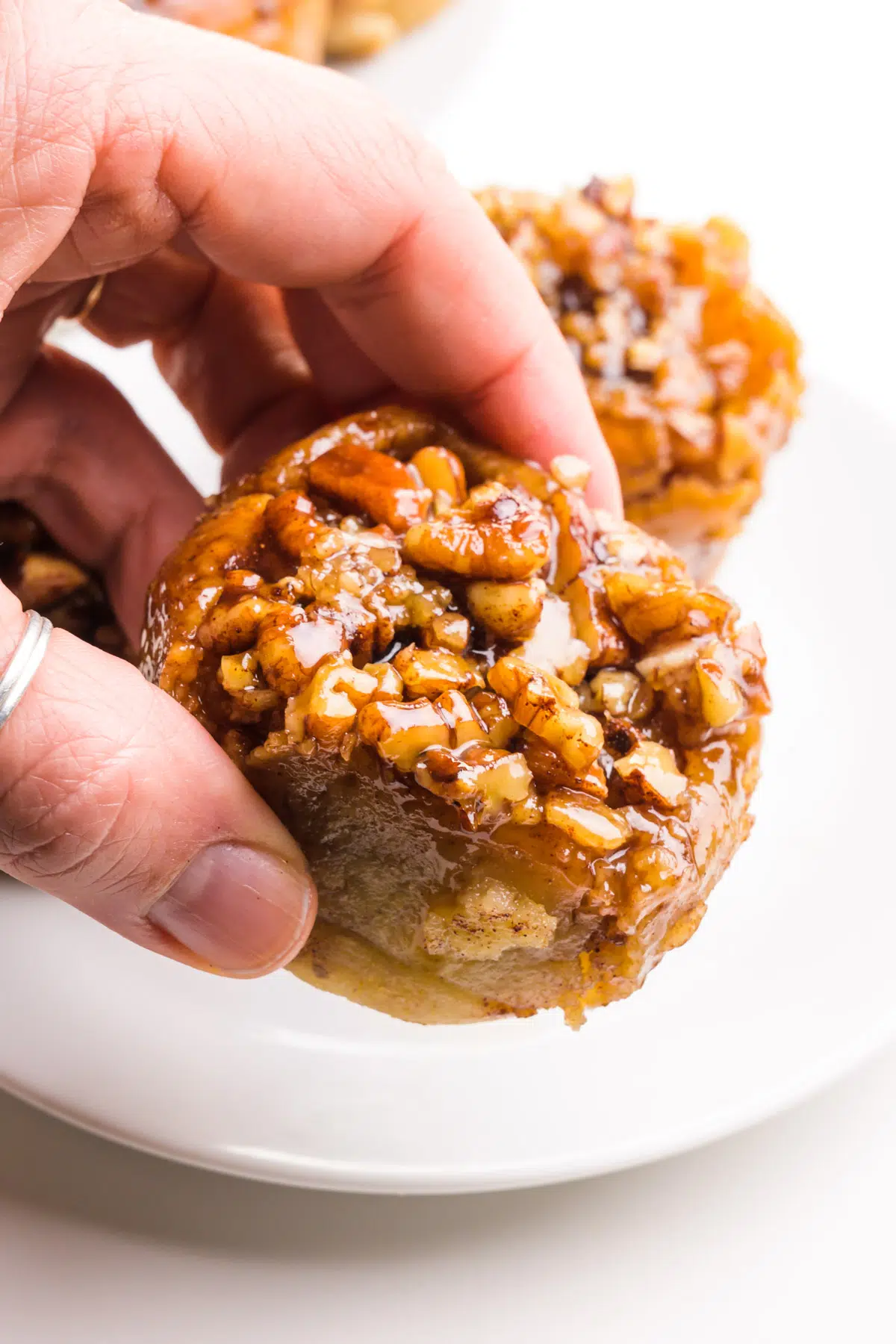A hand holds a gluten-free sticky bun hovering over a plate with more of them.
