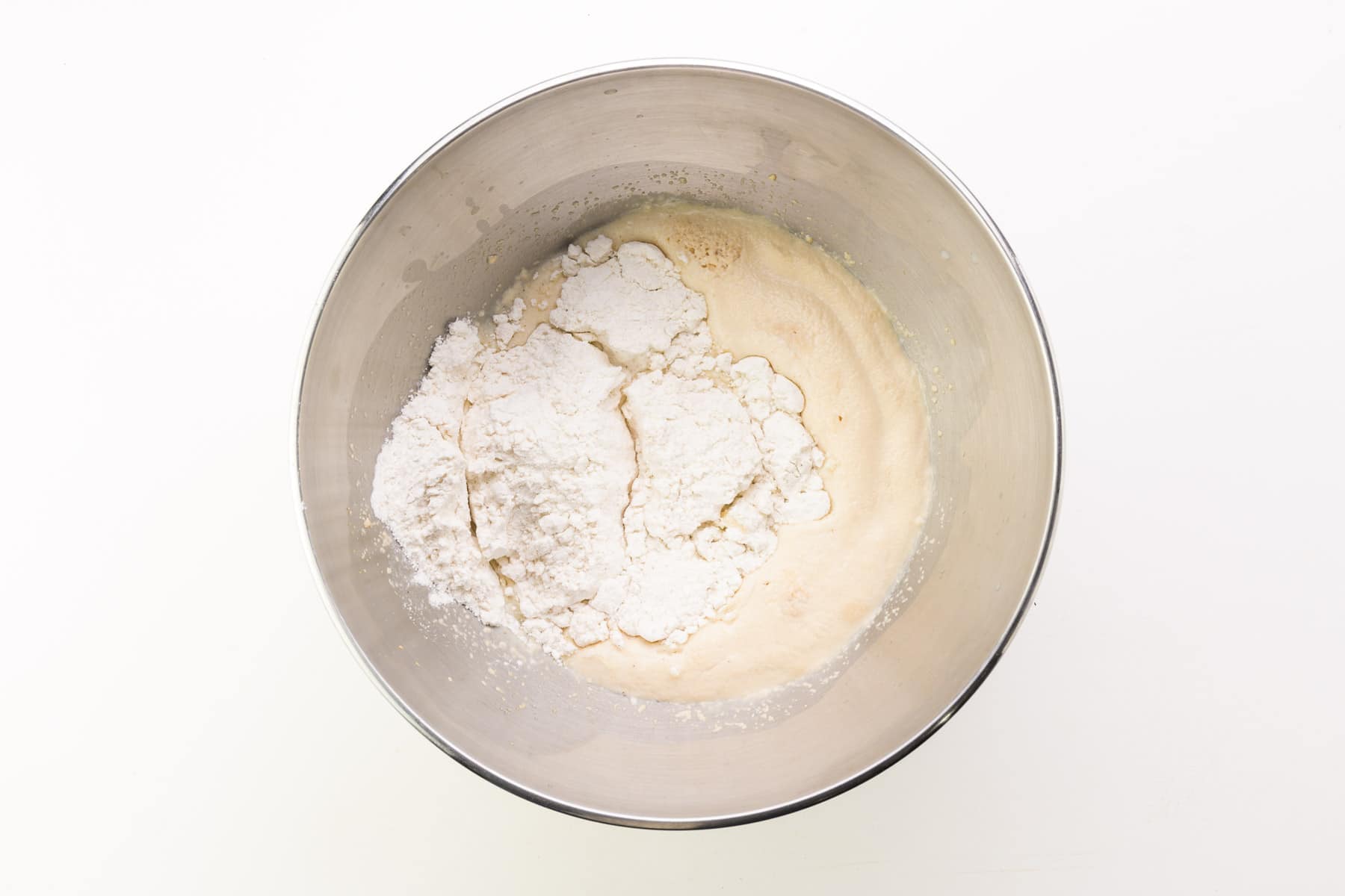 Looking down on a mixing bowl full of a frothy yeast mixture with gluten-free flour added on top.