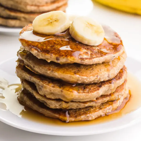 Sliced bananas are on top of a stack of pancakes. There are drizzles of syrup on the pancakes.