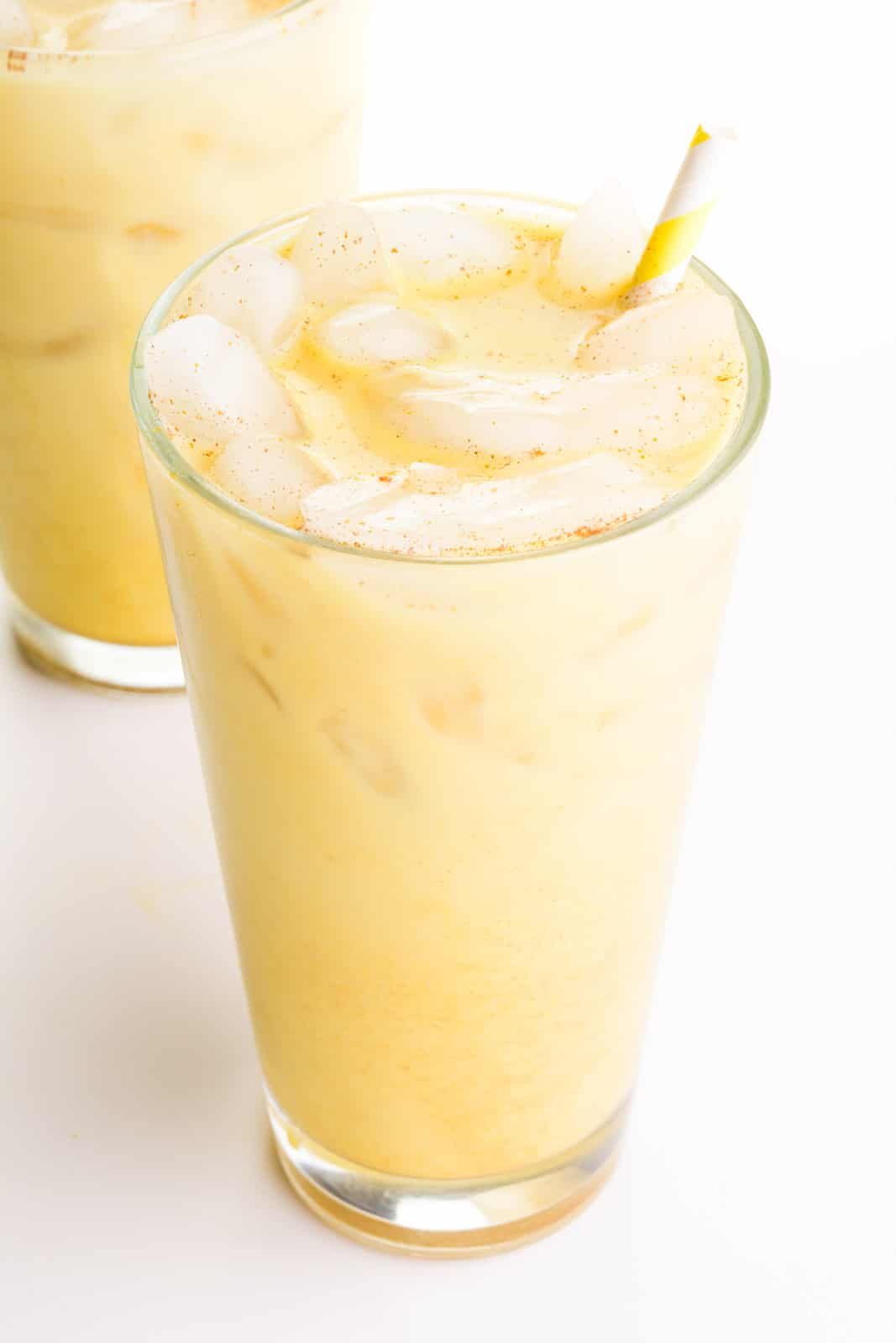 Two glasses, each full of golden milk latte, are sitting one in front of the other. There is a yellow straw in both glasses.