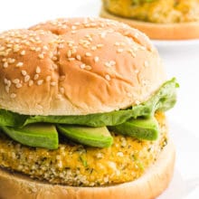 A hemp burger sits on a plate. It has avocado slices and lettuce on it. There's another one on a plate behind it.