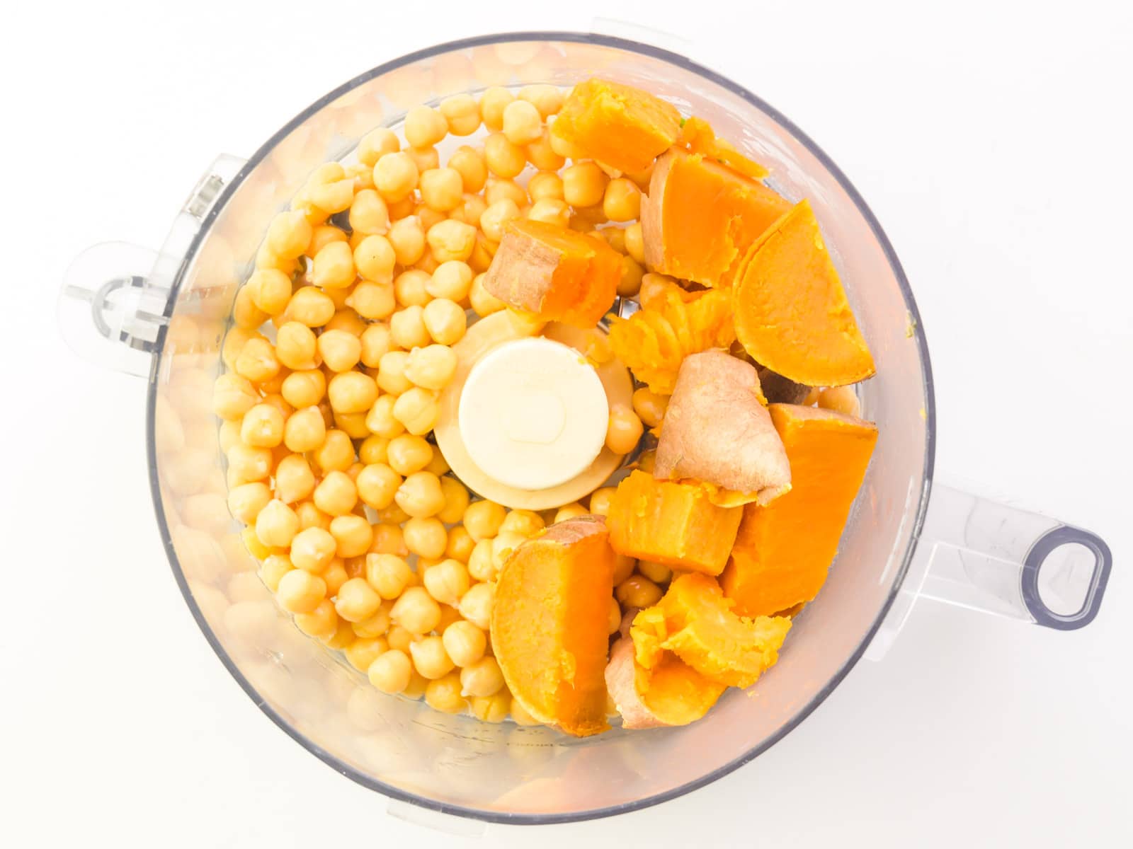 Chickpeas and chopped sweet potatoes are in the bottom of a food processor.