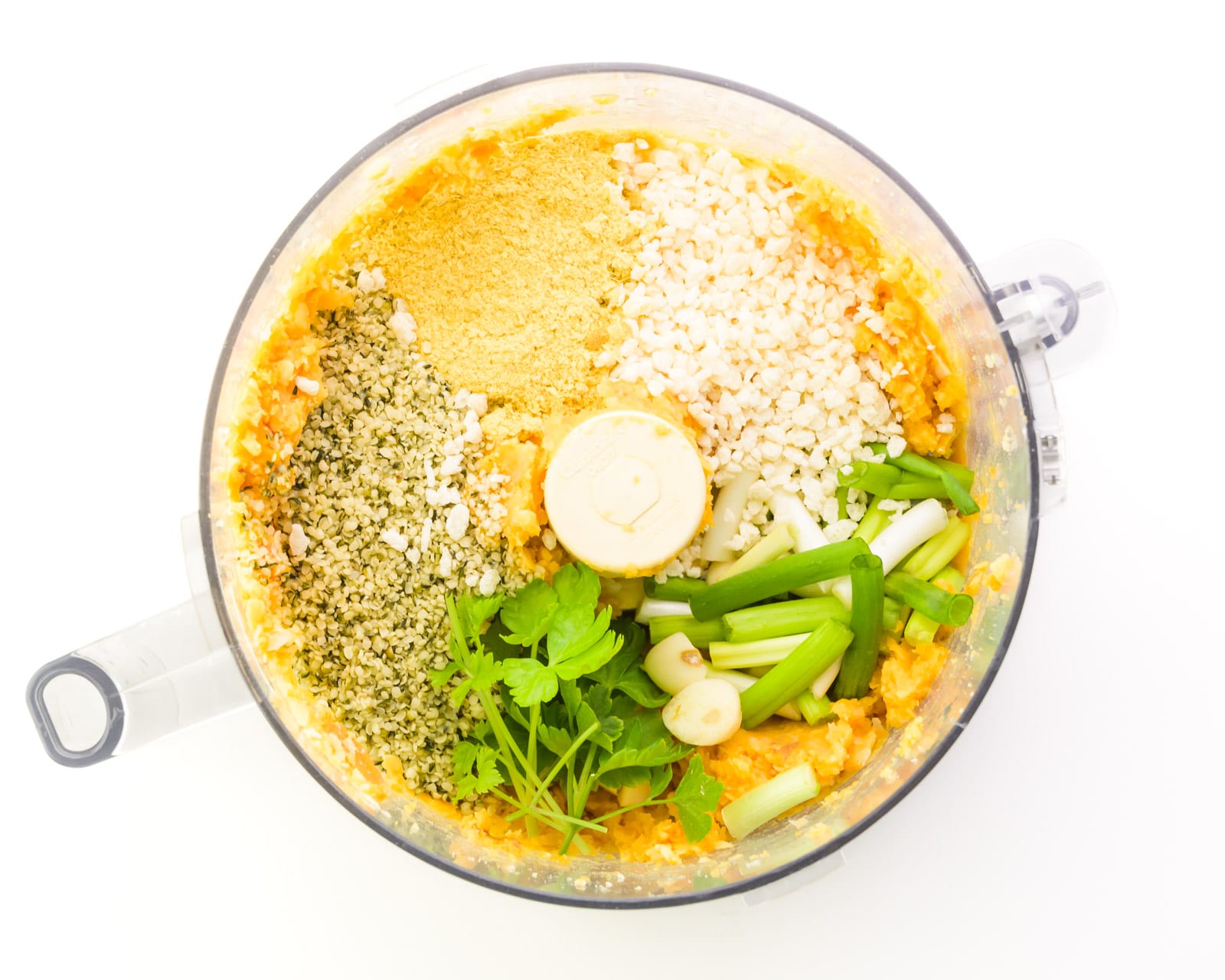 Ingredients are in the bottom of a food processor, including hemp seeds, fresh herbs, breadcrumbs, and more.