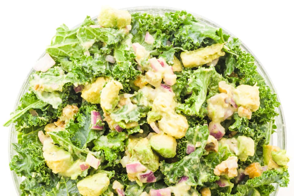 Looking down on a bowl of kale salad with chunks of avocado and walnuts on top.