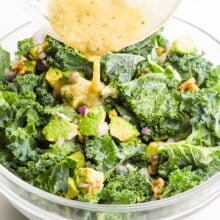 Dressing is being poured over a kale salad.