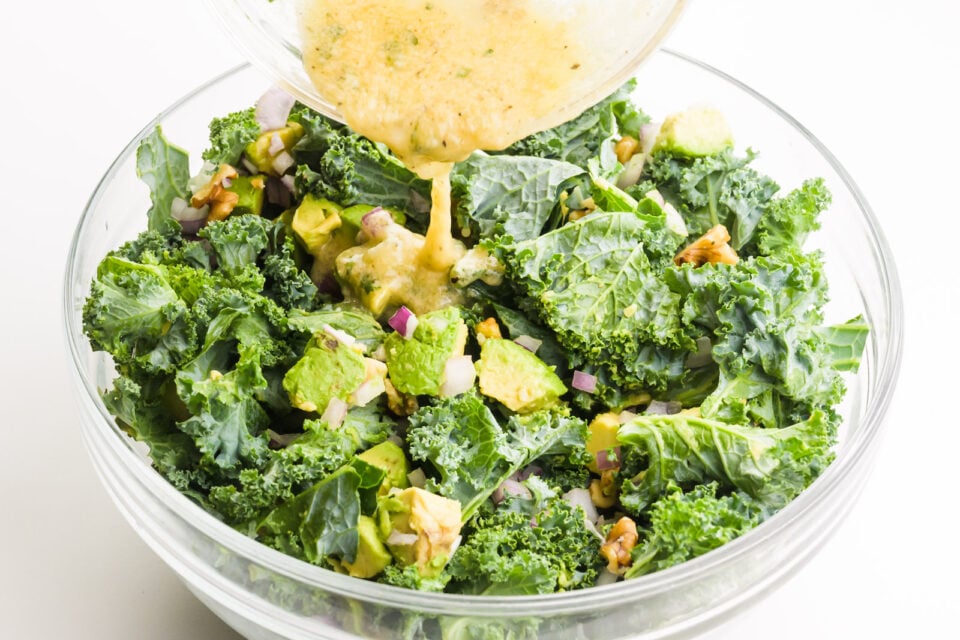 Dressing is being poured over a kale salad.