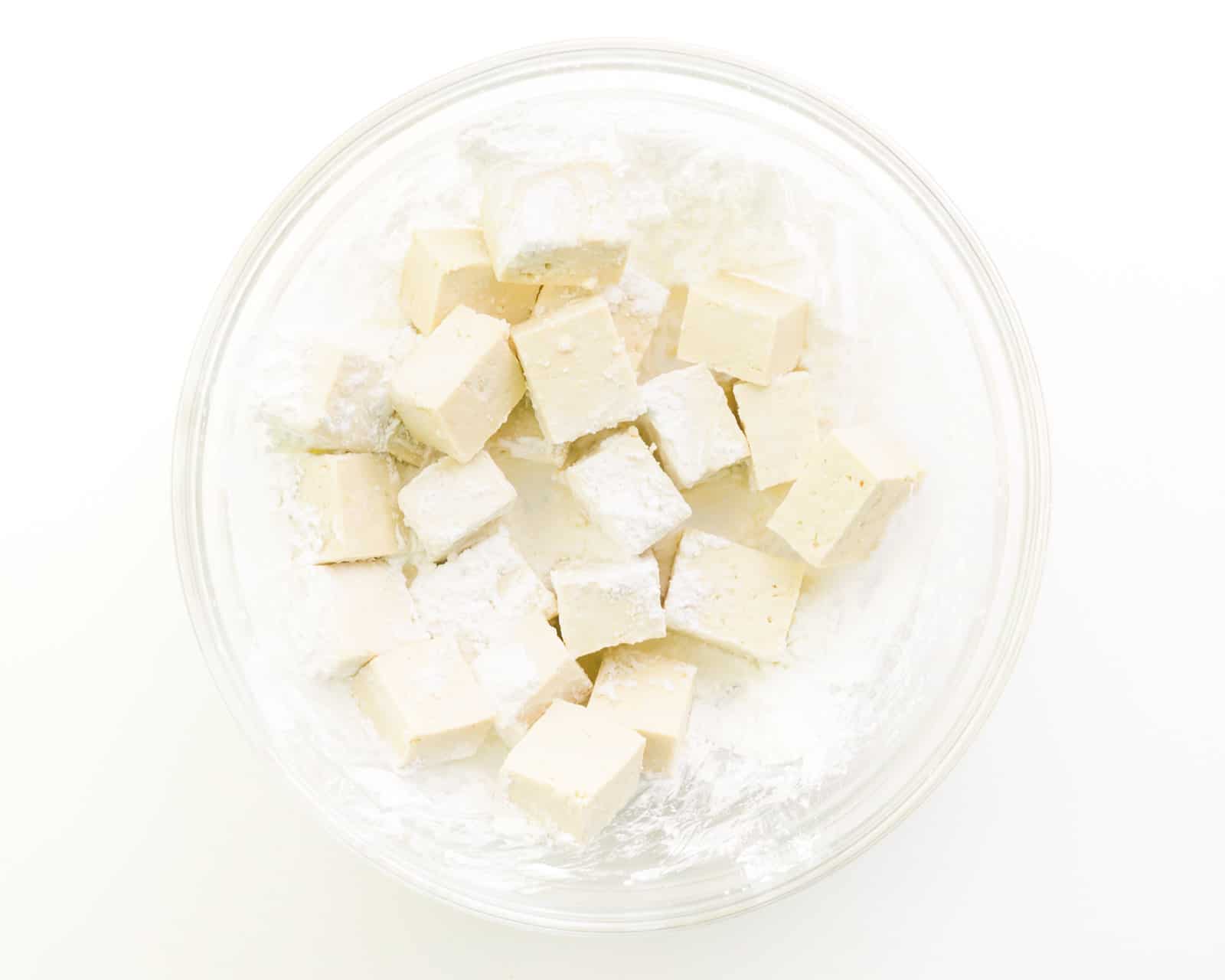 Tofu cubes are surrounded by a cornstarch mixture in the bottom of a bowl.