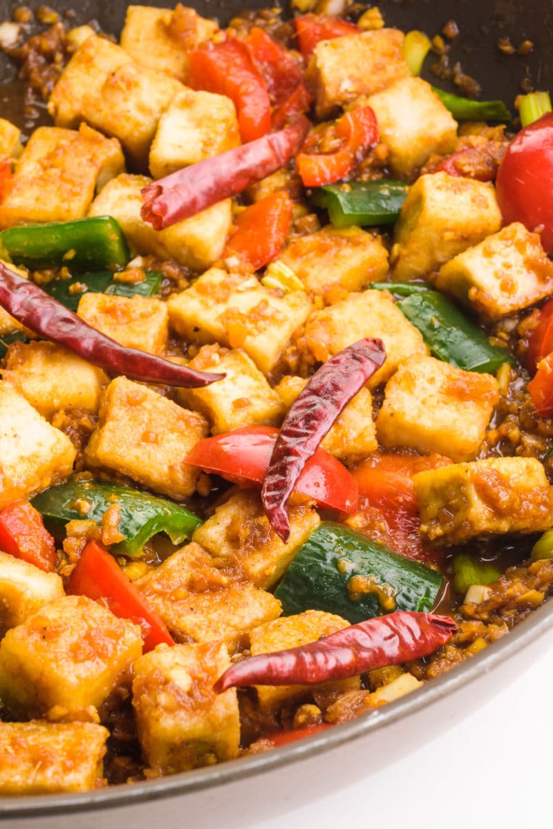A pan holds tofu with vegetables and dried chili peppers.