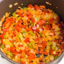 Looking into a saucepan with chopped veggies, such as onions and red bell peppers, being cooked until tender.