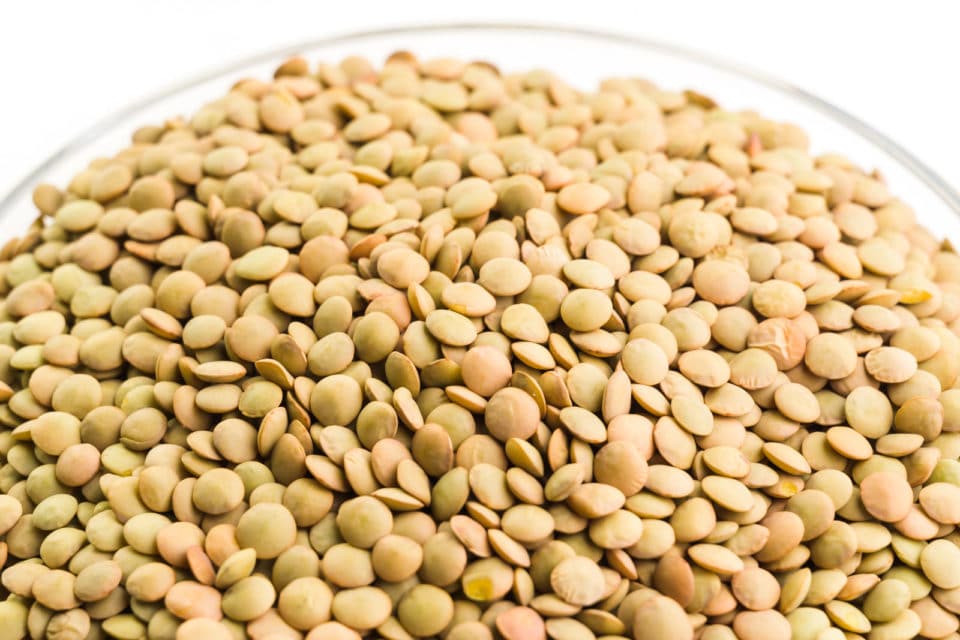 A close-up shot of brown lentils in a glass bowl.