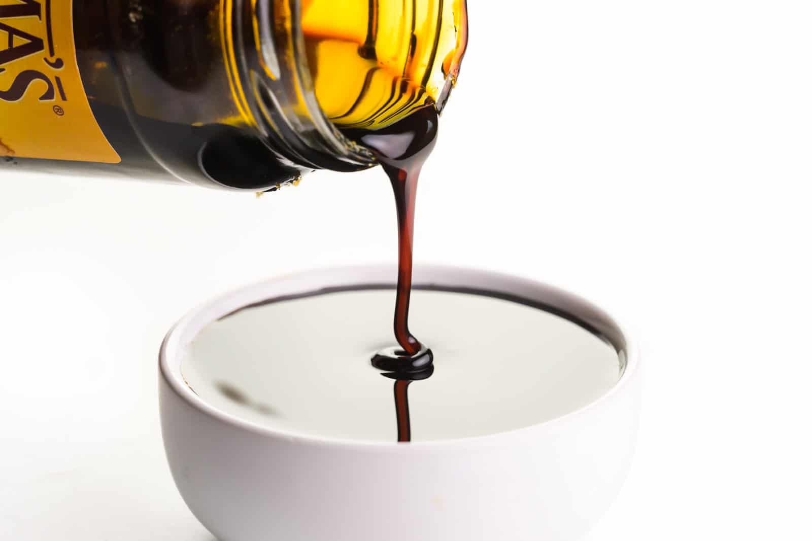 A jar of molasses is pouring into a small white bowl