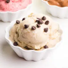 A bowl of vegan nice cream has chocolate chips on top. There are different flavors of ice cream in the background.