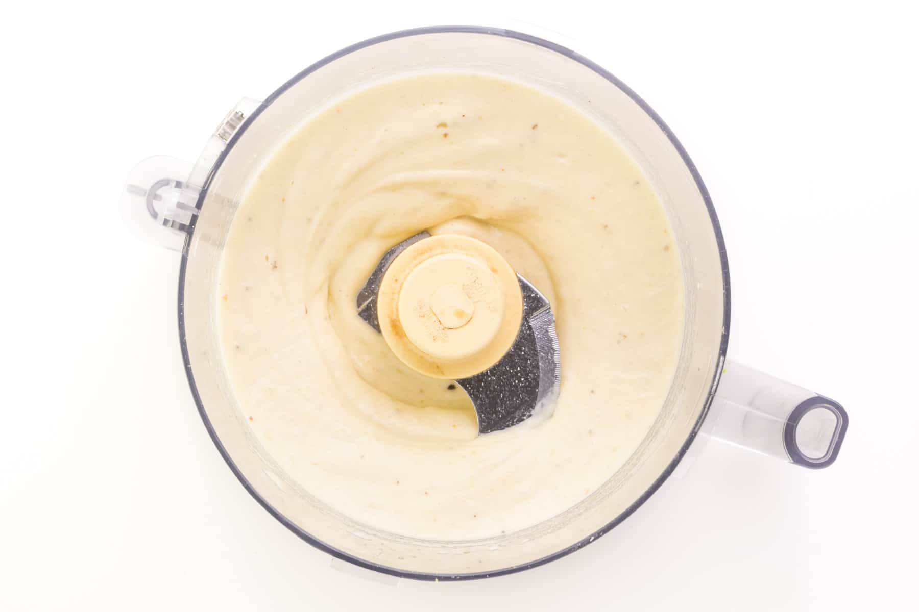 A creamy frozen banana mixture is in the bottom of a food processor bowl.