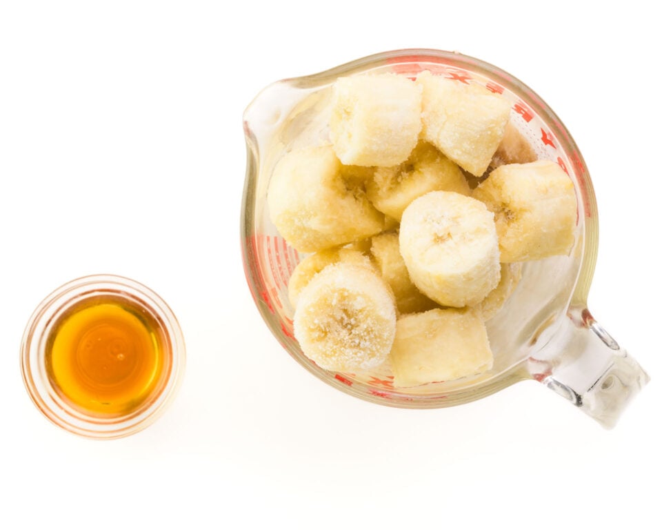 A pyrex measuring glass full of sliced bananas sits next to a small bowl of maple syrup.