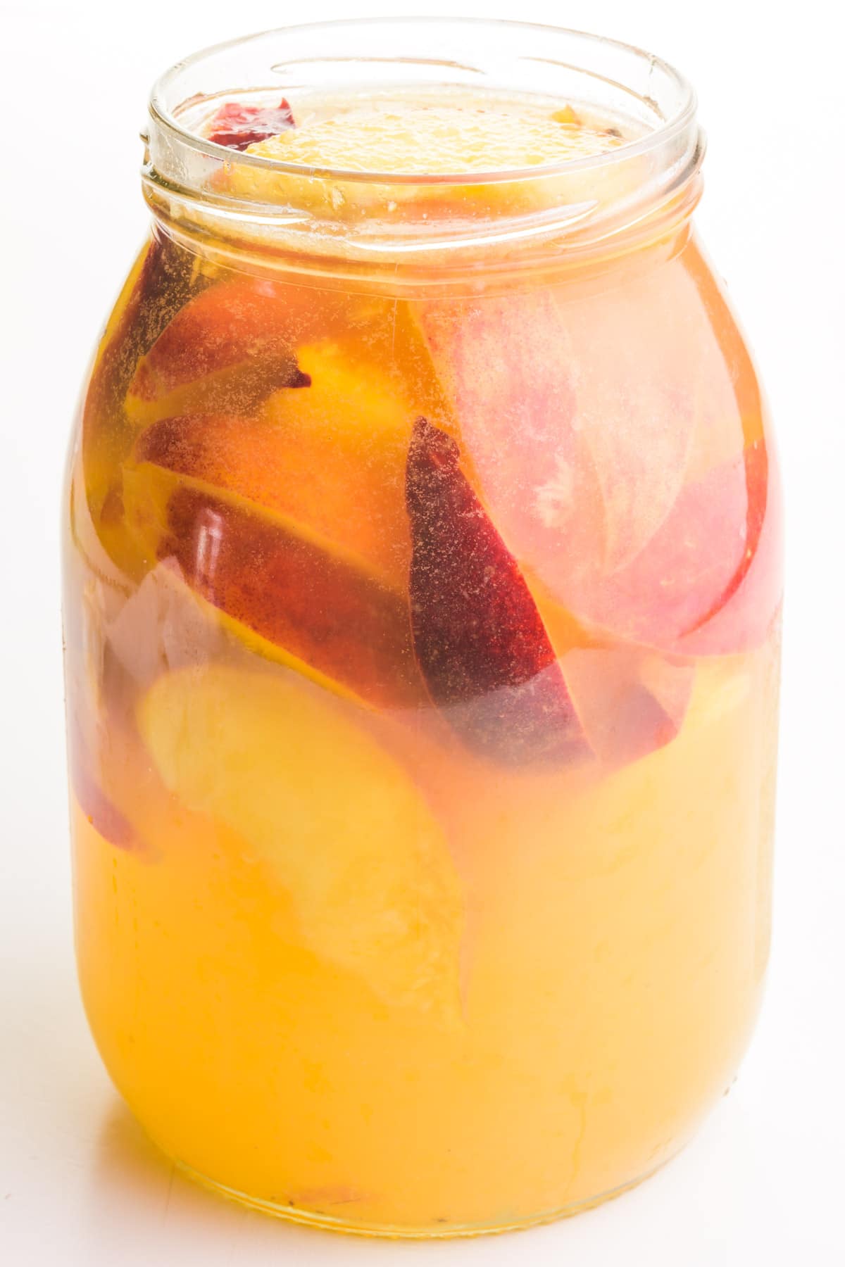 A mason jar holds white win sangria with lots of peach slices.