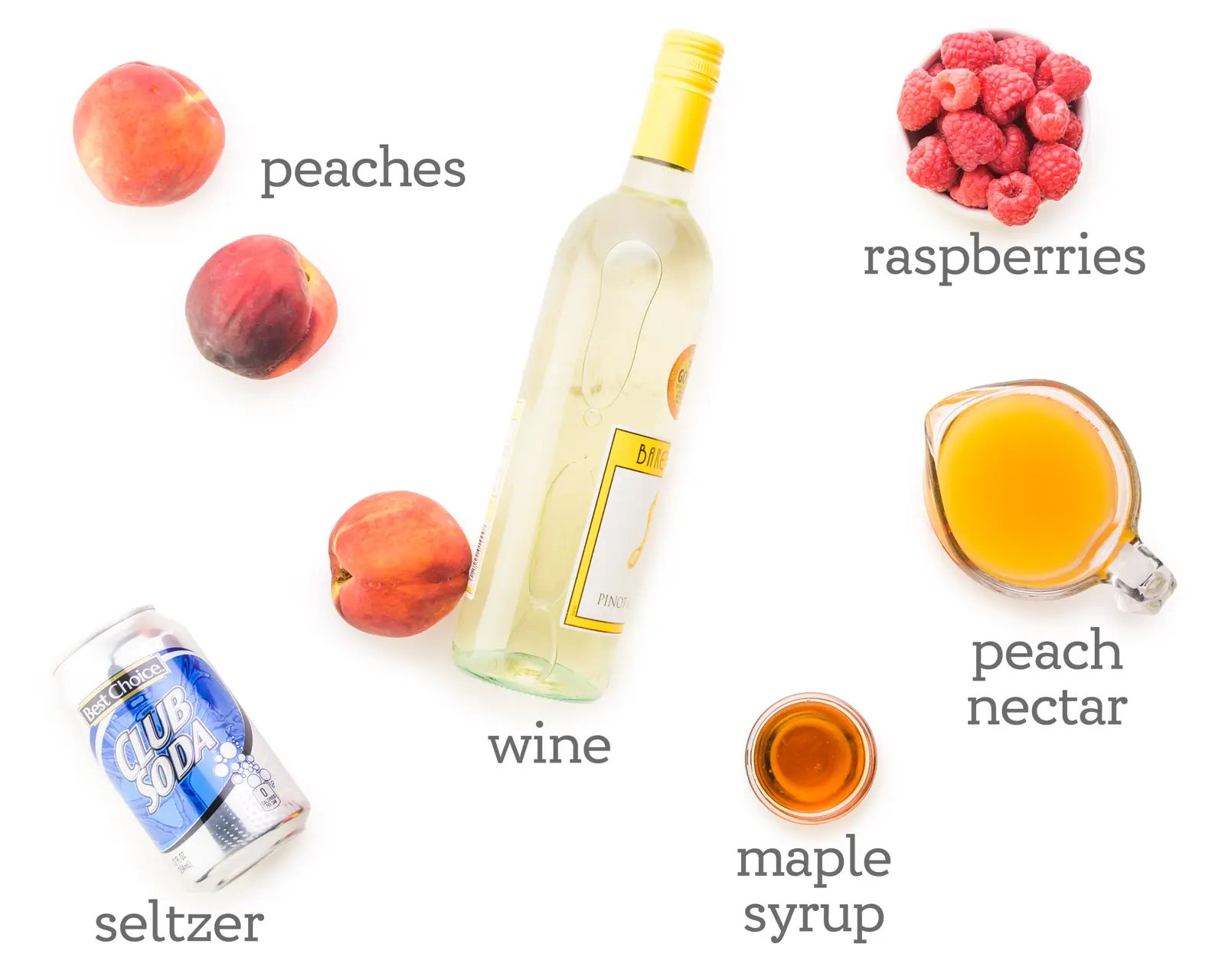 Looking down on a white table with ingredients. The labels next to them read, raspberries, peach nectar, maple syrup, wine, seltzer, and peaches.