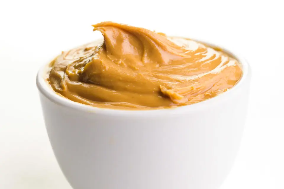 A small, white bowl holds creamy peanut butter inside.