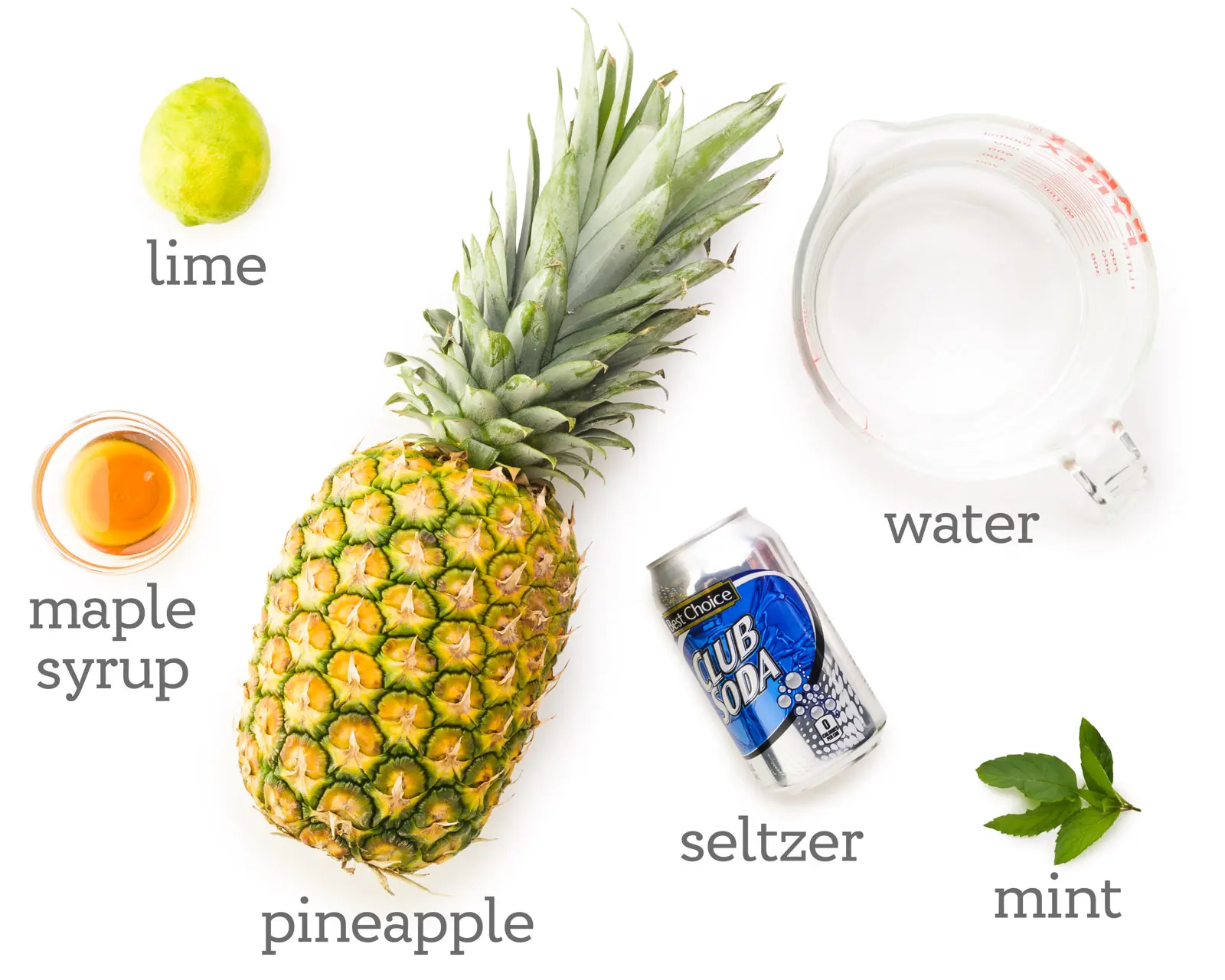 Ingredients are laid out on a white table. The labels next to them read, water, mint, seltzer, pineapple, maple syrup, and lime.