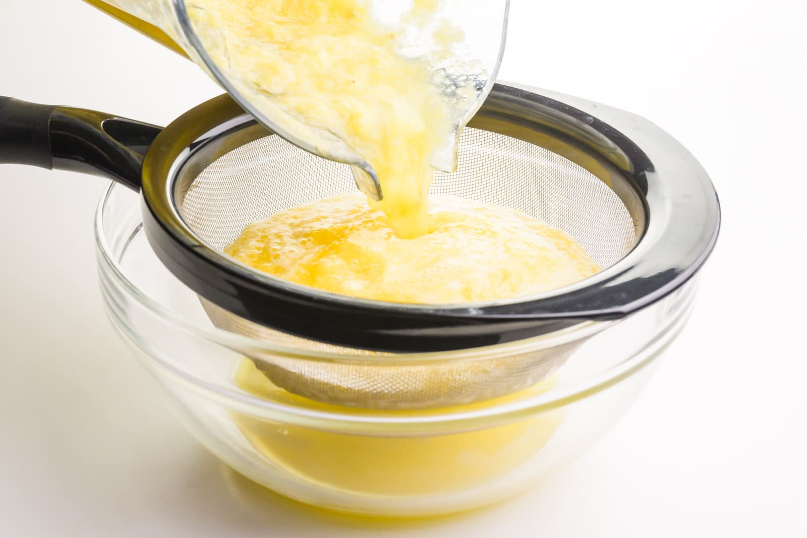 A pineapple slush mixture is being poured into a fine mesh strainer over a bowl, resulting in pineapple juice in the bowl.