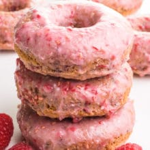 A stack of three donuts has fresh raspberries and more donuts around it and in the background.