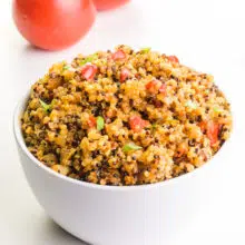 A bowl of Spanish quinoa sits in front of two tomatoes.