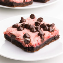 A strawberry chocolate dessert bar sits on a plate. There are more dessert bars on a plate in the background.