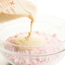 A creamy sauce is being poured into a bowl with strawberry cake mix.