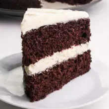 A slice of Vegan Suzy Q Cake sits on a plate. You can see some of the rest of the cake in the background.