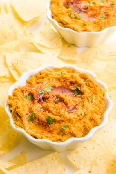 Two bowls hold sweet potato hummus surrounded by tortilla chips.