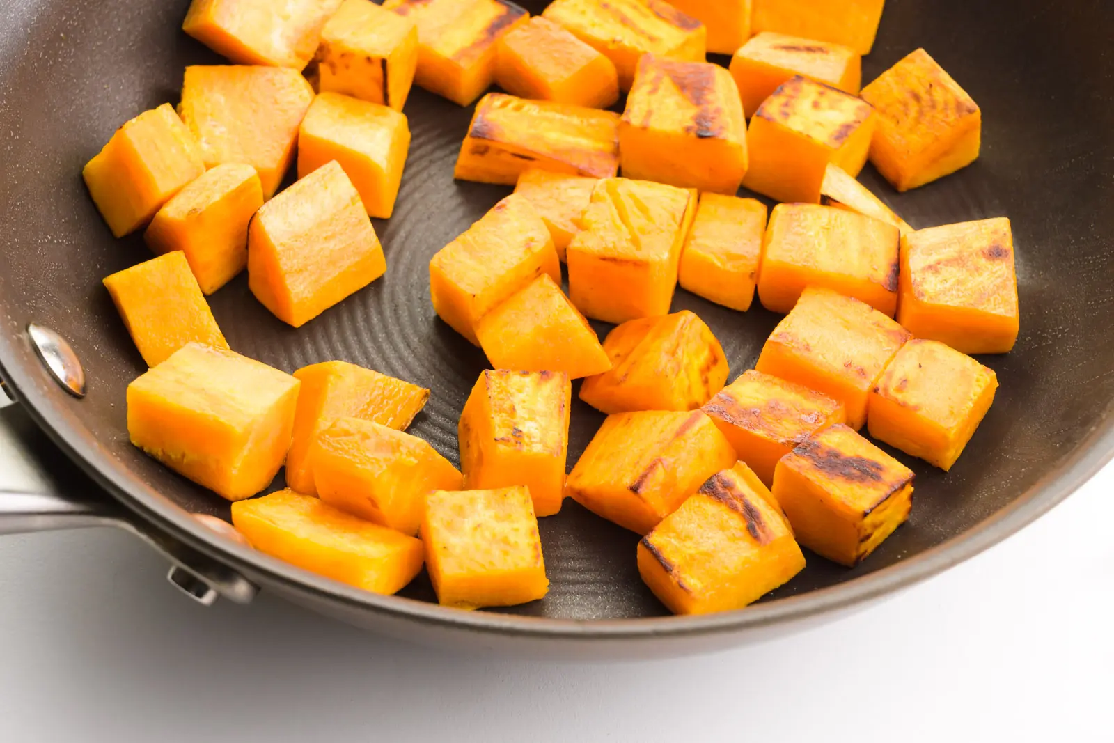 Sweet potato cubes are being sautéed in a skillet.