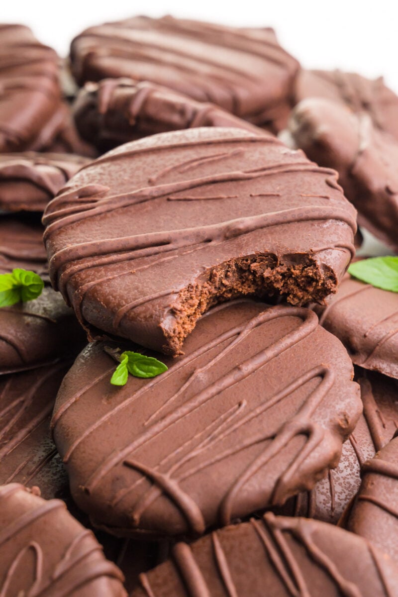 Several chocolate cookies sit on a white table. A bite is taken out of the top cookie.