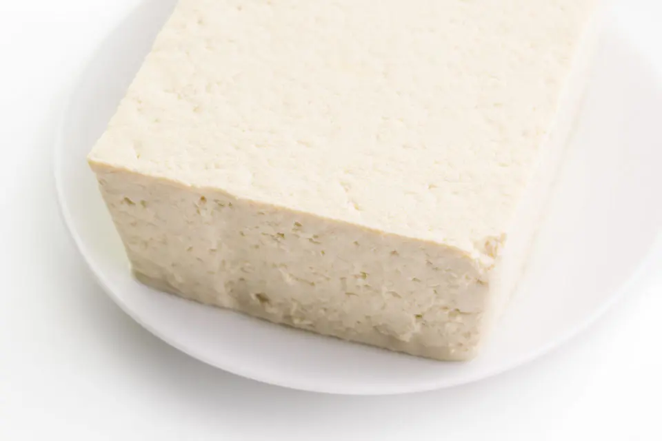 A block of extra firm tofu sits on a white plate.