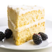 A slice of two-layer vegan vanilla cake with blackberries sitting next to it