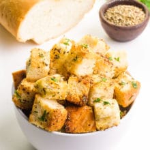 A bowl of croutons sits in front of a bowl of seasonings, herbs, and bread.