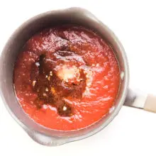 Looking down on a saucepan with a tomato sauce mixture with other ingredients ready to be stirred together.