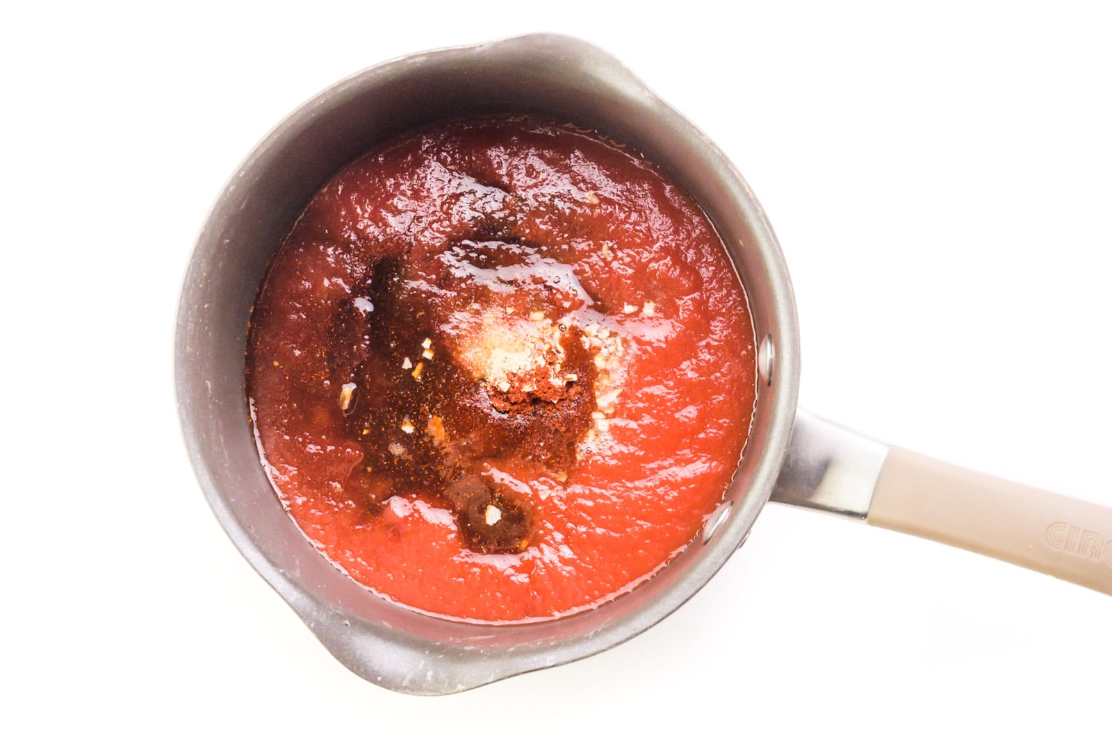 Looking down on a saucepan with a tomato sauce mixture with other ingredients ready to be stirred together.