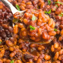 A spoon holds a serving of vegan baked beans hovering over over the rest of the dish full of it.