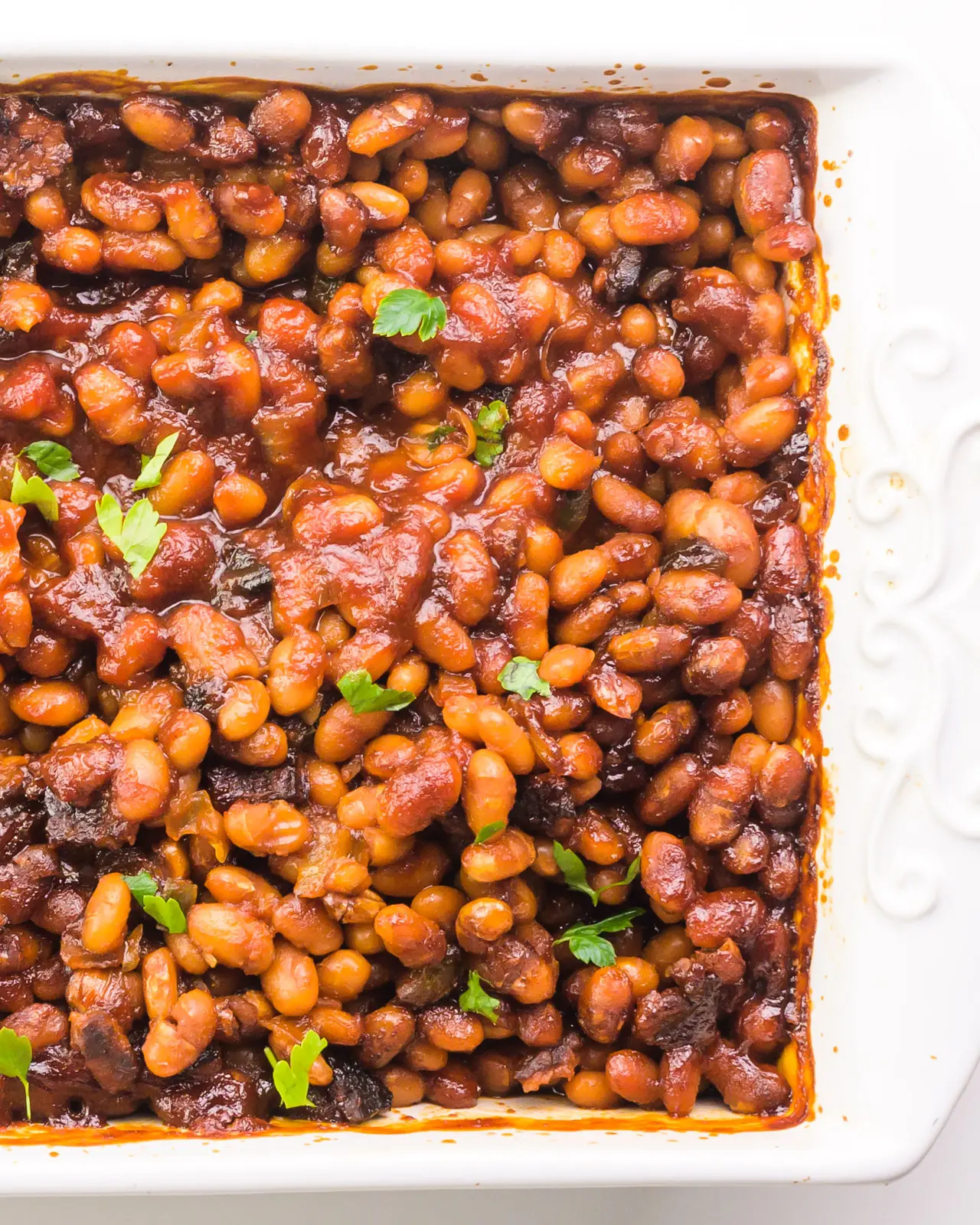 Looking down into a white baking dish full of baked beans with fresh chopped parsley on top.