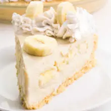 A slice of vegan banana cream pie sits on a plate. It has sliced bananas and coconut whipped cream on top.