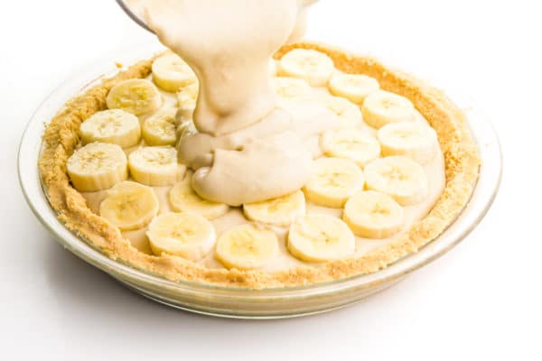 Vanilla pudding is being poured on top of a pie with pudding and banana slices on top.