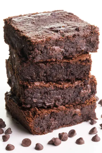 A stack of vegan black bean brownies has chocolate chips sitting around it.