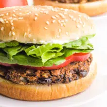 A vegan black bean burger sits on a bun with toppings like sliced tomatoes and greens.