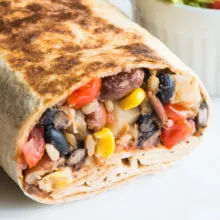 Close up of a Crispy Black Bean Burrito cut open showing black beans, pinto beans, tomato, corn and diced potatoes