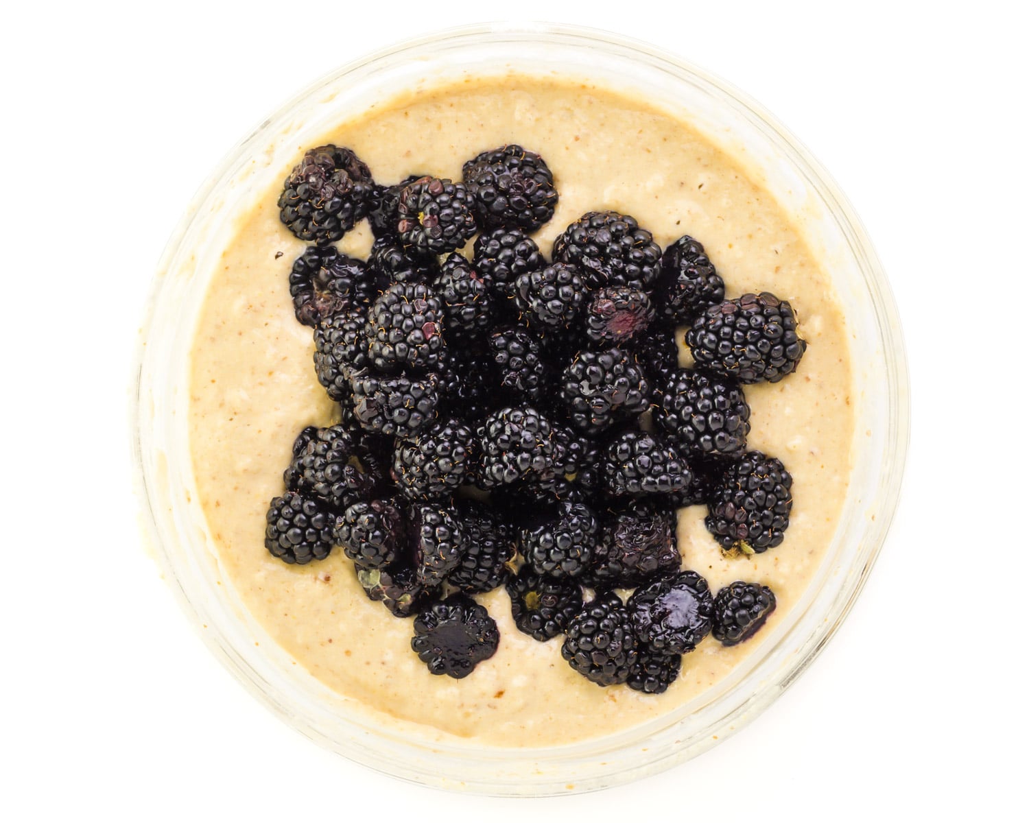 Looking down on a bowl of muffin batter with fresh blackberries on top.
